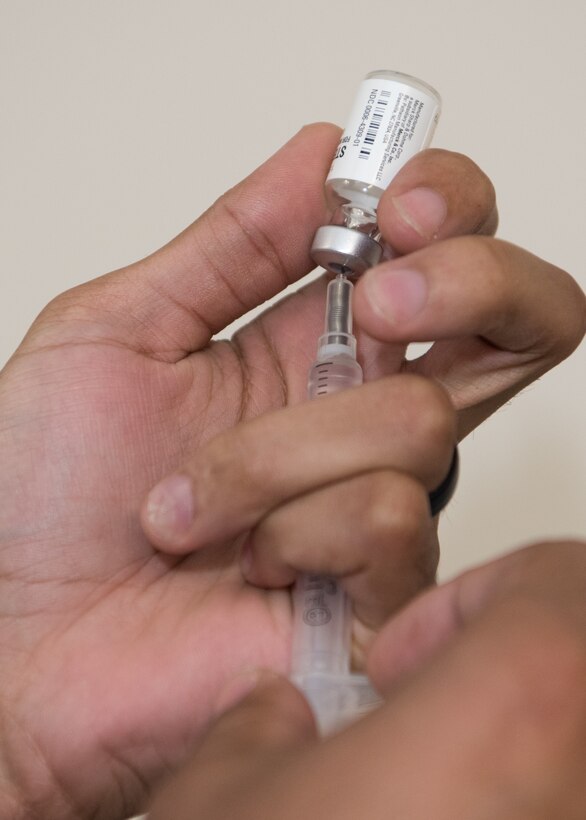U.S. Air Force Staff Sgt. Bradley Debrick, 509th Medical Operations Squadron immunizations technician, fills a syringe with medicine from a glass bottle.