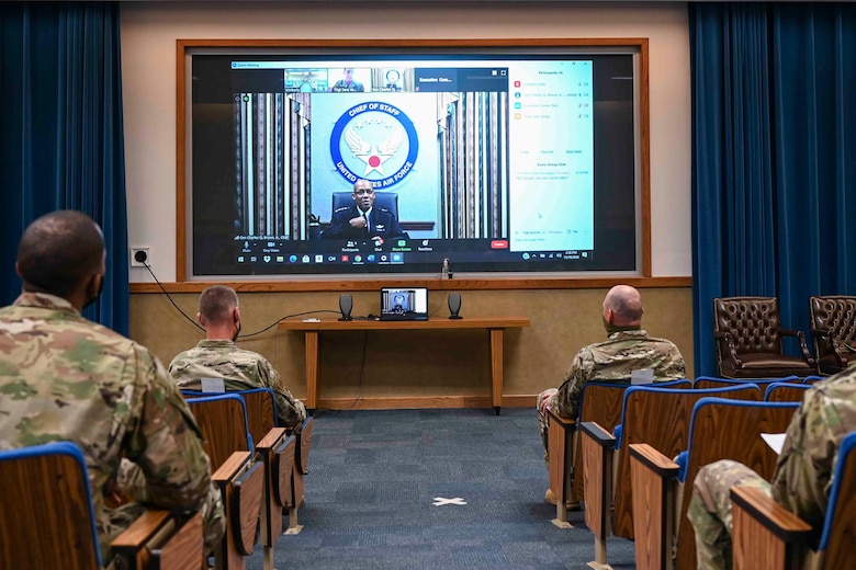 Airmen sitting in an auditorium listening to a virtual speaker