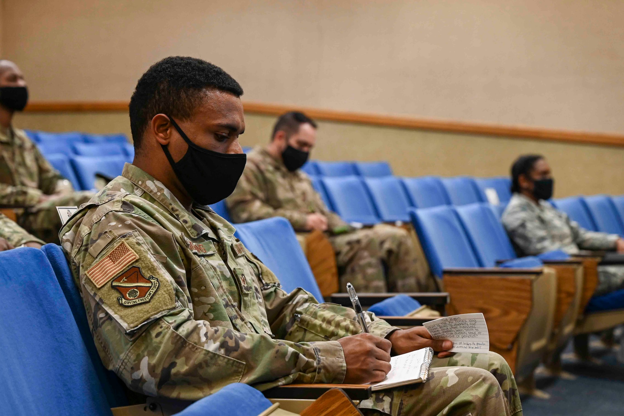 Airmen sitting in an auditorium listening to a virtual speaker