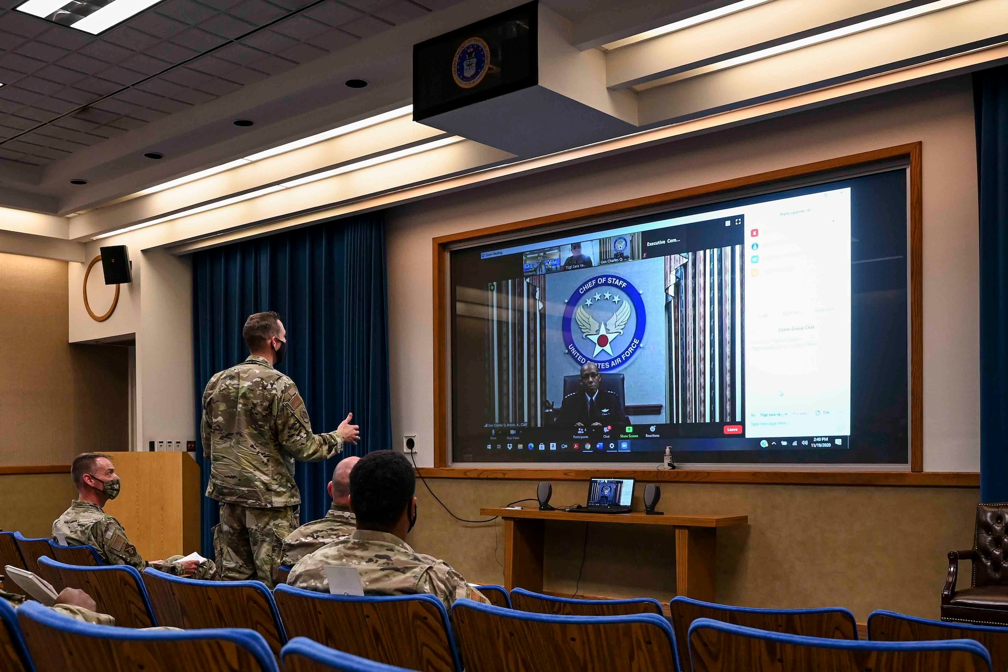 Airmen sitting in an auditorium listening to a virtual speaker
