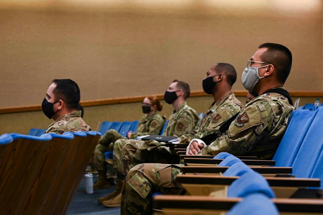 Airmen sitting in an auditorium listen to a speaker.