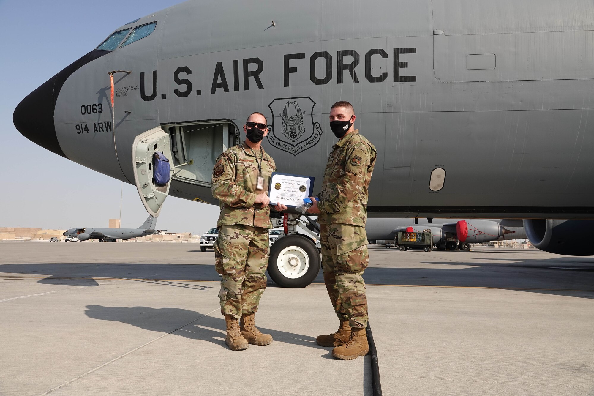 U.S. Air Force Lt. Col. Dennis Warburton, acting 379th Expeditionary Aircraft Maintenance Squadron commander, presents U.S. Air Force Airman 1st Class Trever Van Oss, with the 379th Expeditionary Logistics Readiness Squadron, with a certificate after his crew chief for a day experience on Nov. 17, 2020, at Al Udeid Air Base, Qatar. Van Oss helped launch a KC-135 Stratotanker aircraft alongside maintenance Airmen, marshalled it into a parking spot and serviced the engine oil after the aircraft shut down. The crew chief for a day program provides interested Airmen of any military specialty, direct exposure to the 379th Air Expeditionary Wing's robust aerial refueling capability. (Photo courtesy of the U.S. Air Force) (ID badge obscured for OPSEC)