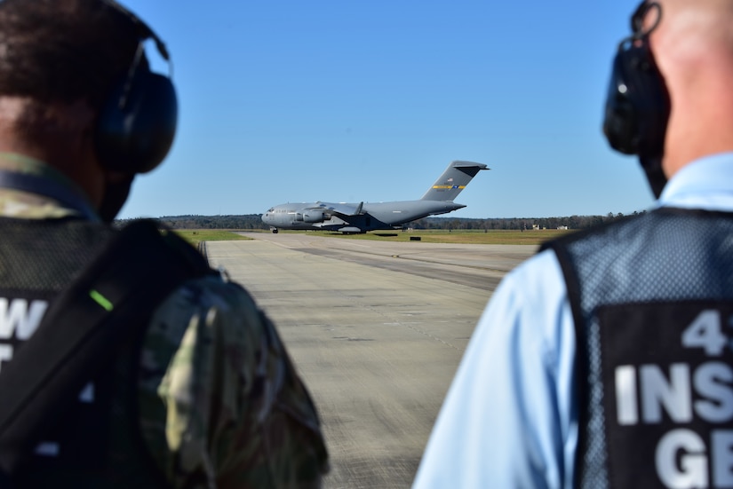 U.S. Air Force Master Sgt. Bradley Moorer, an Inspector General Wing Inspection Team superintendent for the 437th Airlift Wing (right), and Mark Vickers, the 437th AW IG director of inspections (left), monitor Airmen offloading cargo from a C-17 Globemaster III, at McEntire Joint National Guard Base, S.C., Nov. 16, 2020. Palmetto Challenge is a global mobilization exercise held at McEntire Joint National Guard Base, S.C. The exercise is held in order to develop readiness and awareness in a simulated deployed environment for over 100 Airmen from Joint Base Charleston.