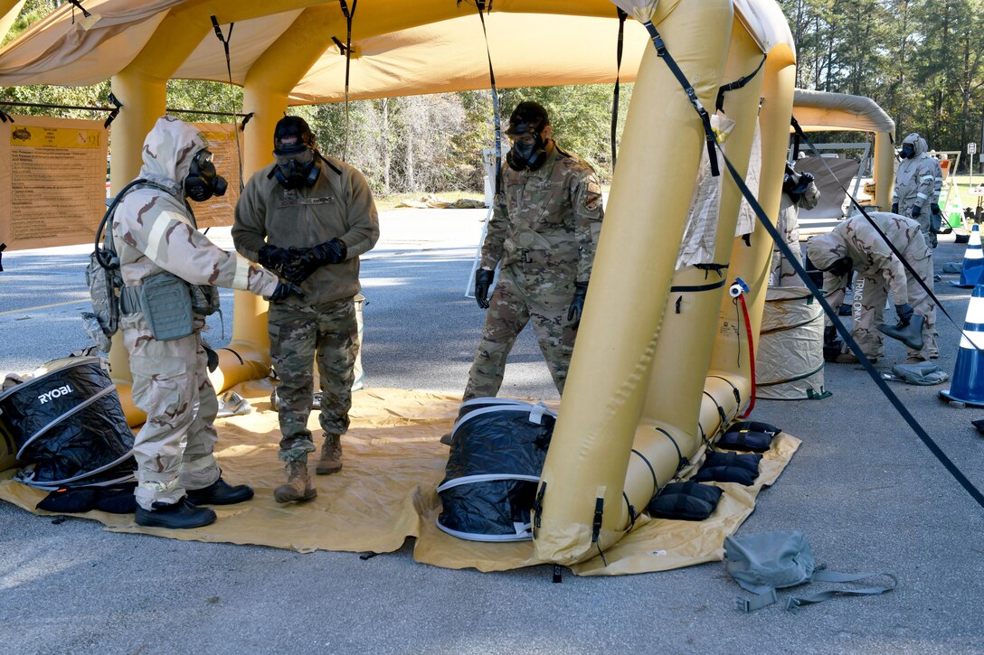 Photo shows Airmen walking through a tent removing their chemical gear.