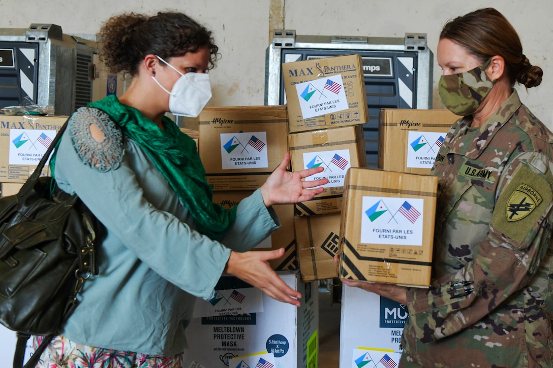 A soldier wearing a face mask gives a box to a civilian wearing a face mask.