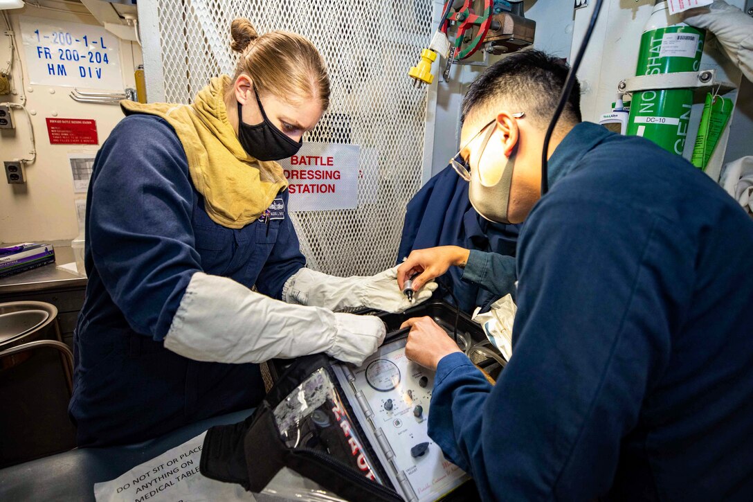 Two sailors wearing protective gear work on a device.