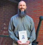 IMAGE: DAHLGREN, Va. – Michael Brown holds a New Testament translated into the Algonquin language by English Puritan missionary John Eliot and printed in 1661. As a Naval Surface Warfare Center Dahlgren Division branch head and the command’s Native American Indian and Alaska Native Special Emphasis Program Manager, Brown strives to make a positive impact for Dahlgren’s employees. “I am thankful for the opportunity to serve in both of these capacities to help each person fulfill their purpose in their community, at NSWC Dahlgren Division and for the Navy.”  (U.S. Navy photo/Released)