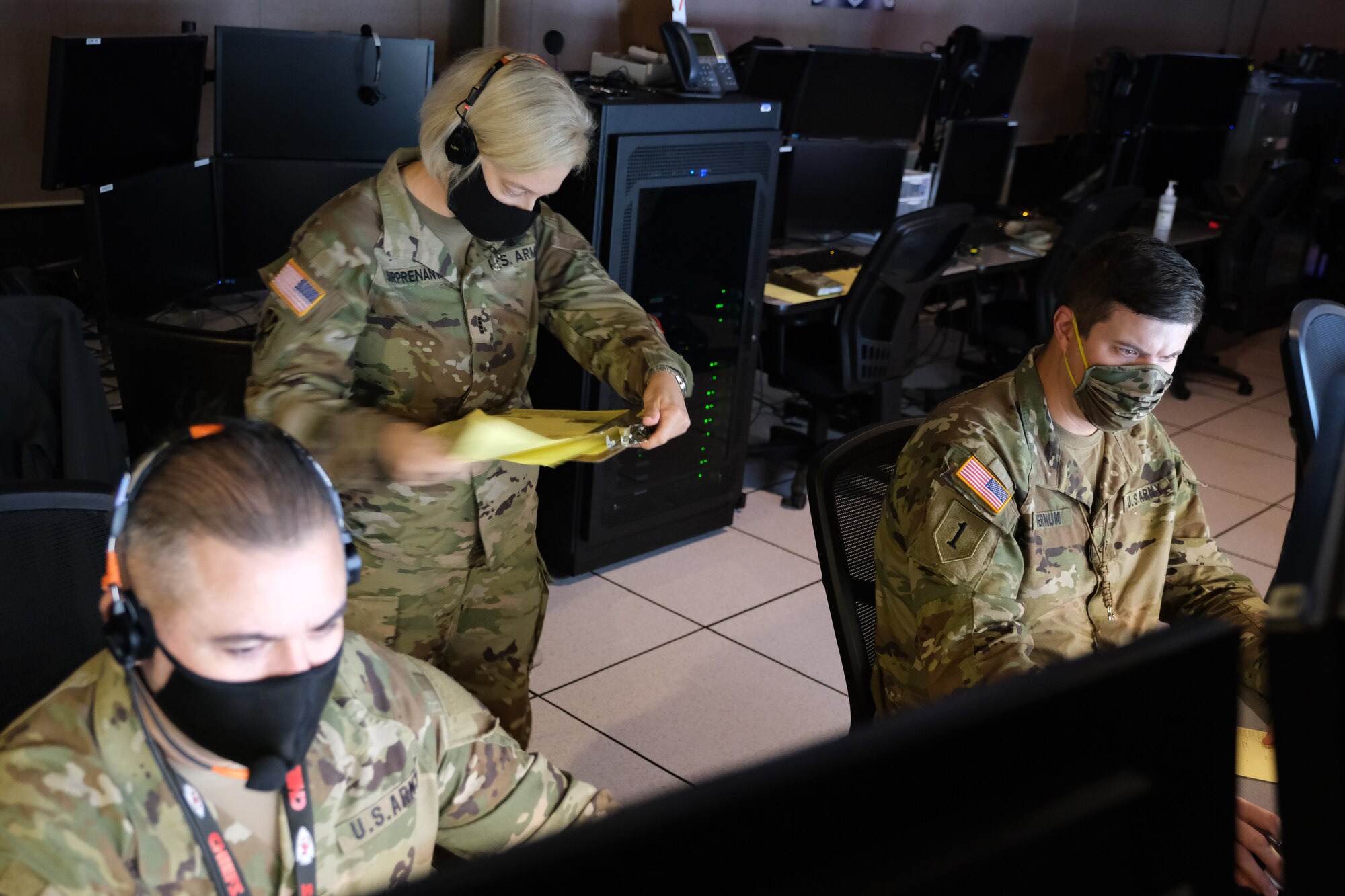 Two U.S. Army personnel sitting at computers and one female U.S. Army warrant officer standing behind them.