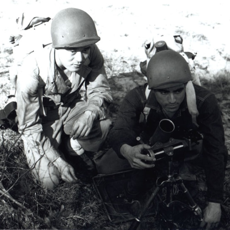 Two men set up a mortar launcher on the ground.