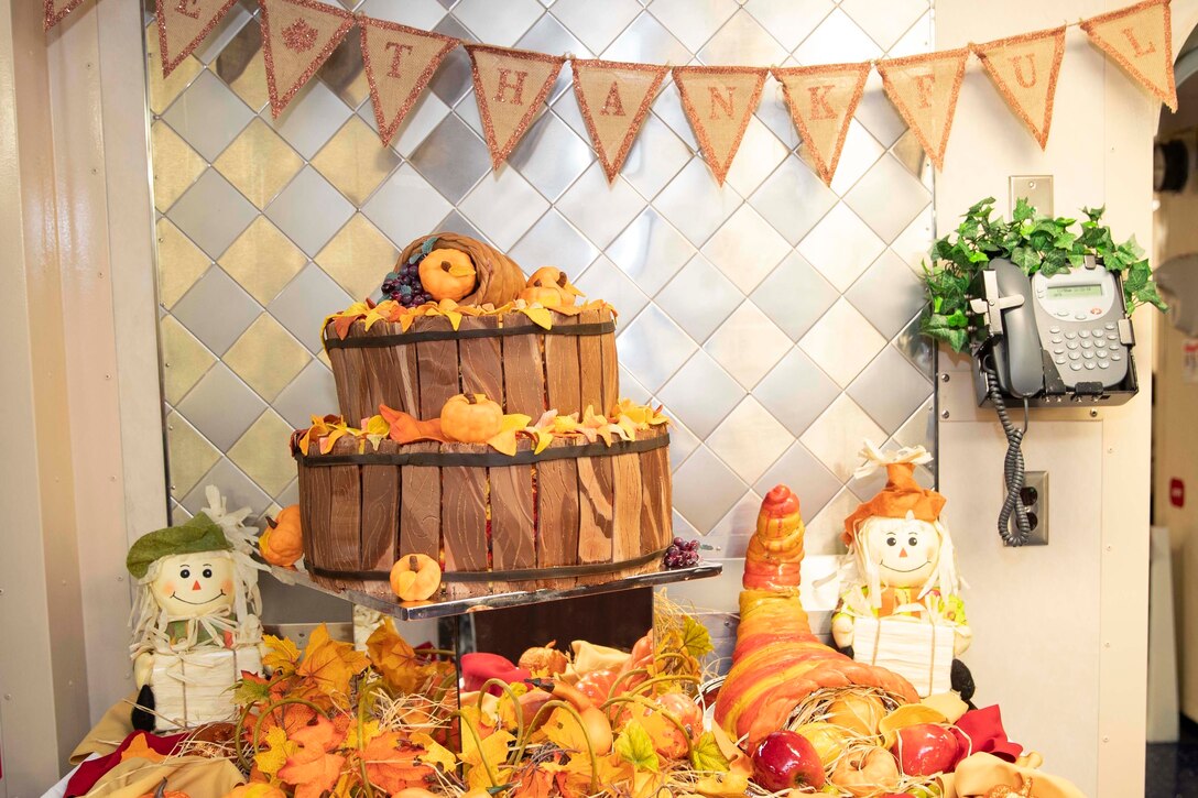A table filled with fall decorations is under a sign that says, "Be Thankful."
