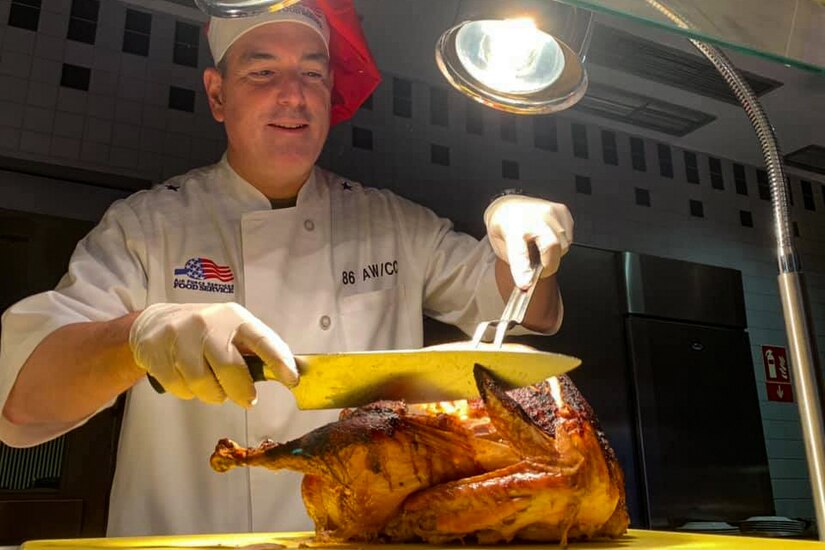 A chef carves a turkey under bright lights.