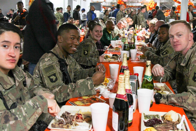 Soldiers sit together at a long table and enjoy a meal.