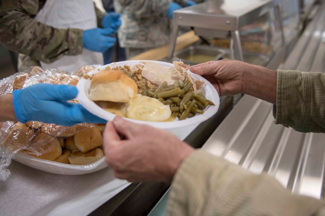 Two hands receive a food-filled plate from a server.