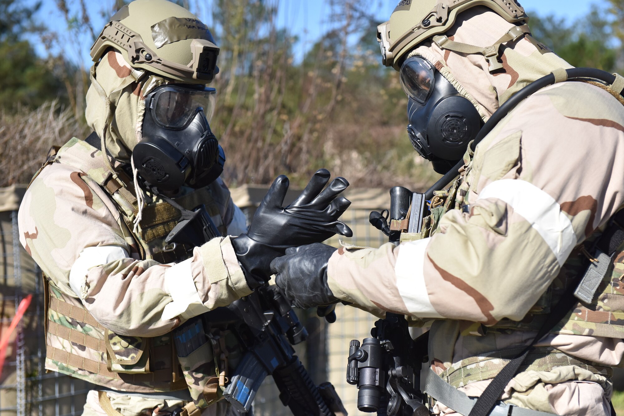 Photo shows Airmen in chemical gear putting on gloves.