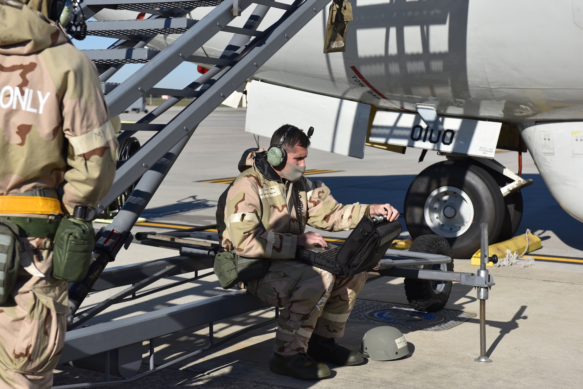 Photo shows an Airman sitting next to an aircraft on a laptop.