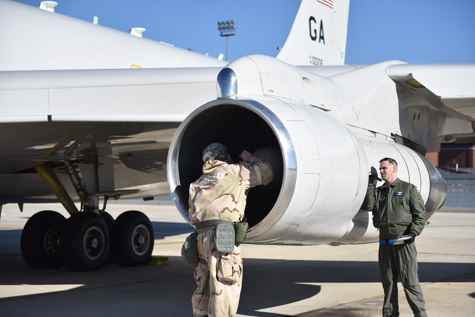 Photo shows two Airmen using flashlights to check the intake of an aircraft.