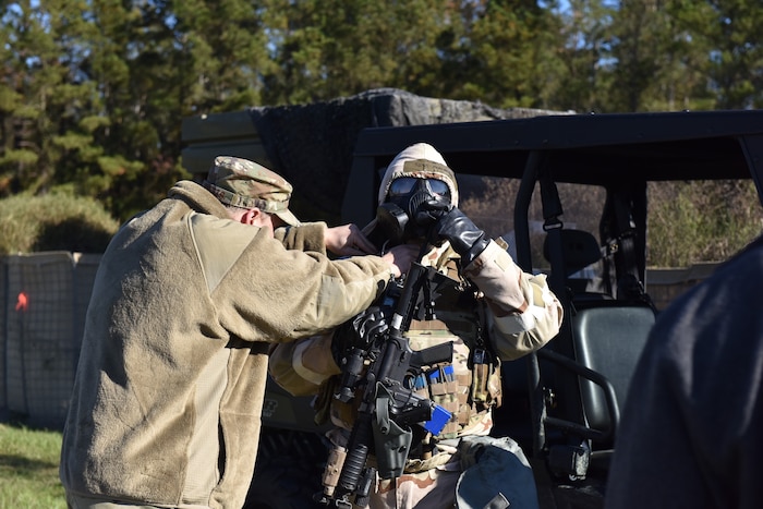 Photo shows one Airman checking the seal of a gas mask on another Airman.