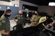 Three U.S. Air Force officers stand in front of computer screens.