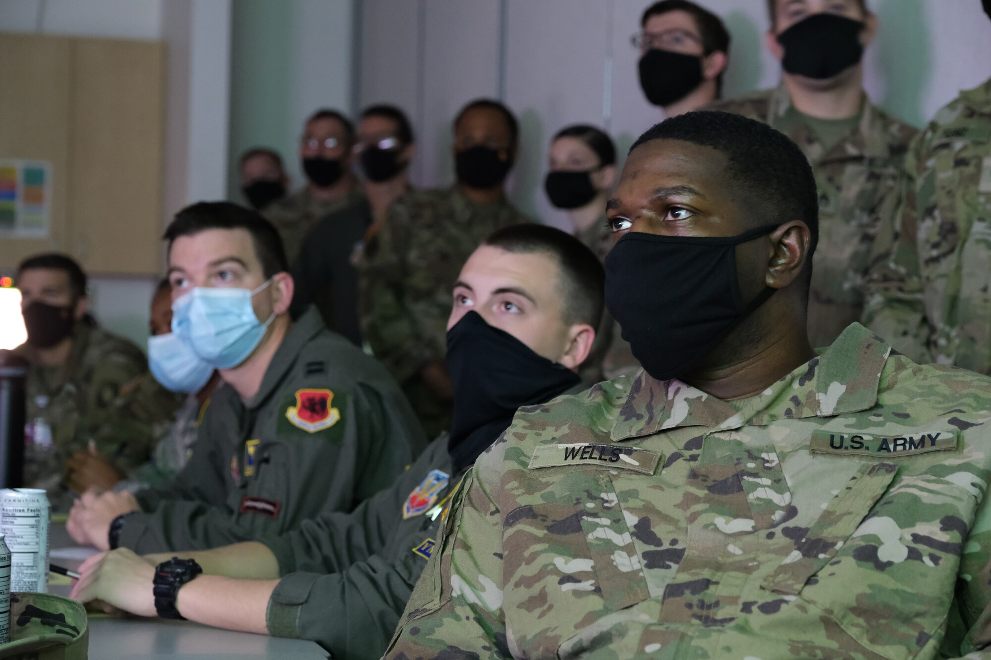 Military personnel in uniform seated at a table and military standing behind the table all wearing face masks.