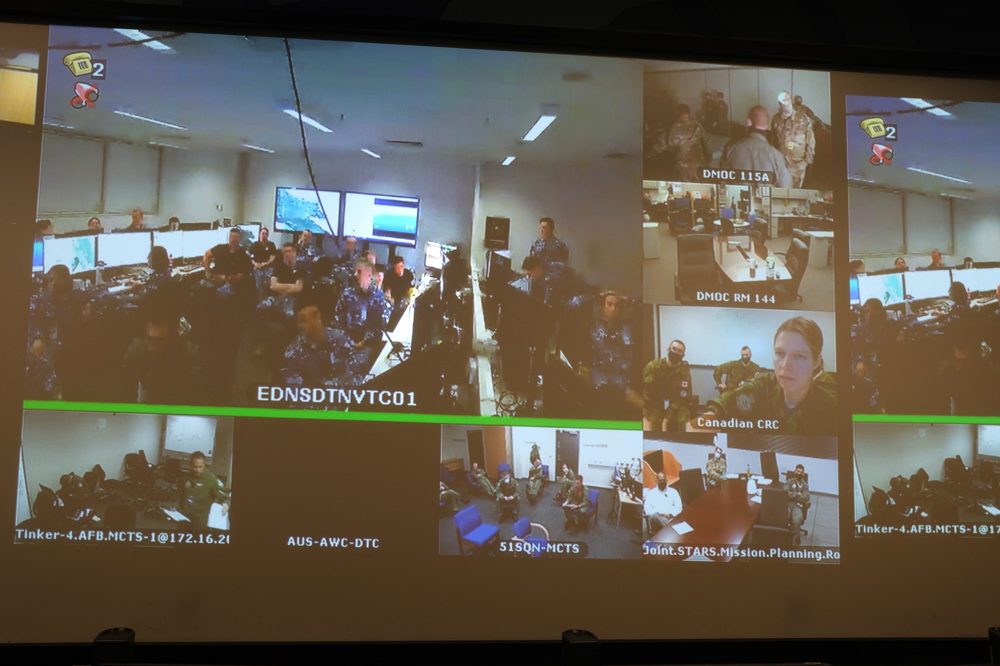 Photo of video screen with multiple locations of U.S. and Coalition forces sitting at tables.