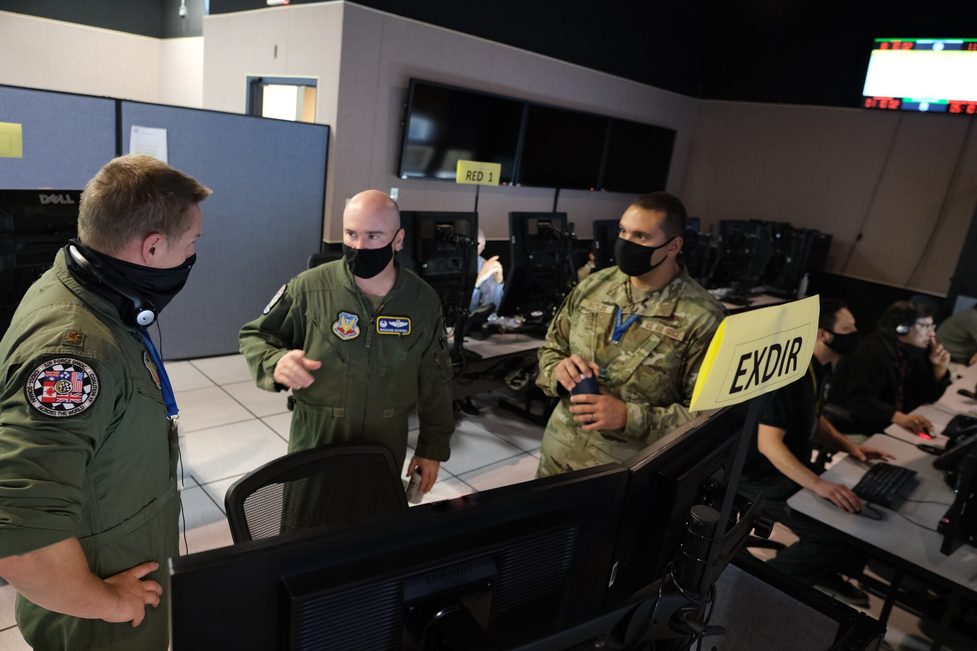 Three U.S. Air Force officers stand in front of computer screens.