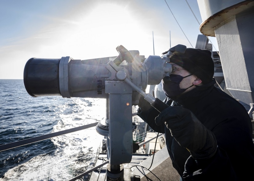 A sailor looks into a telescope on the bridge of a ship.