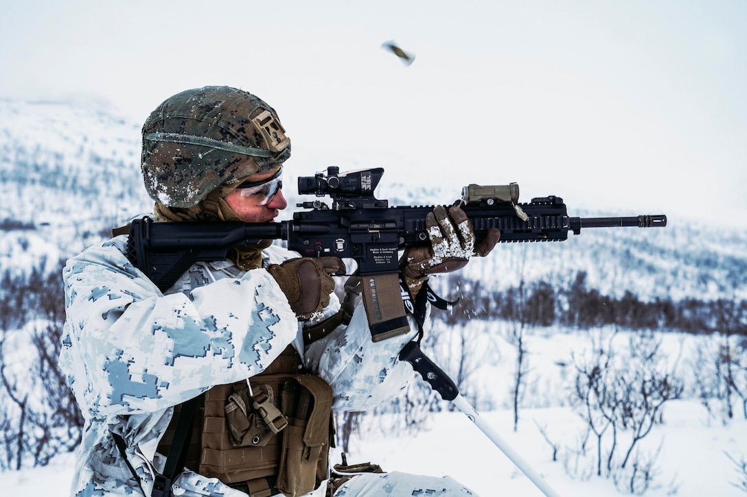A Marine fires a weapon in a snowy forest.