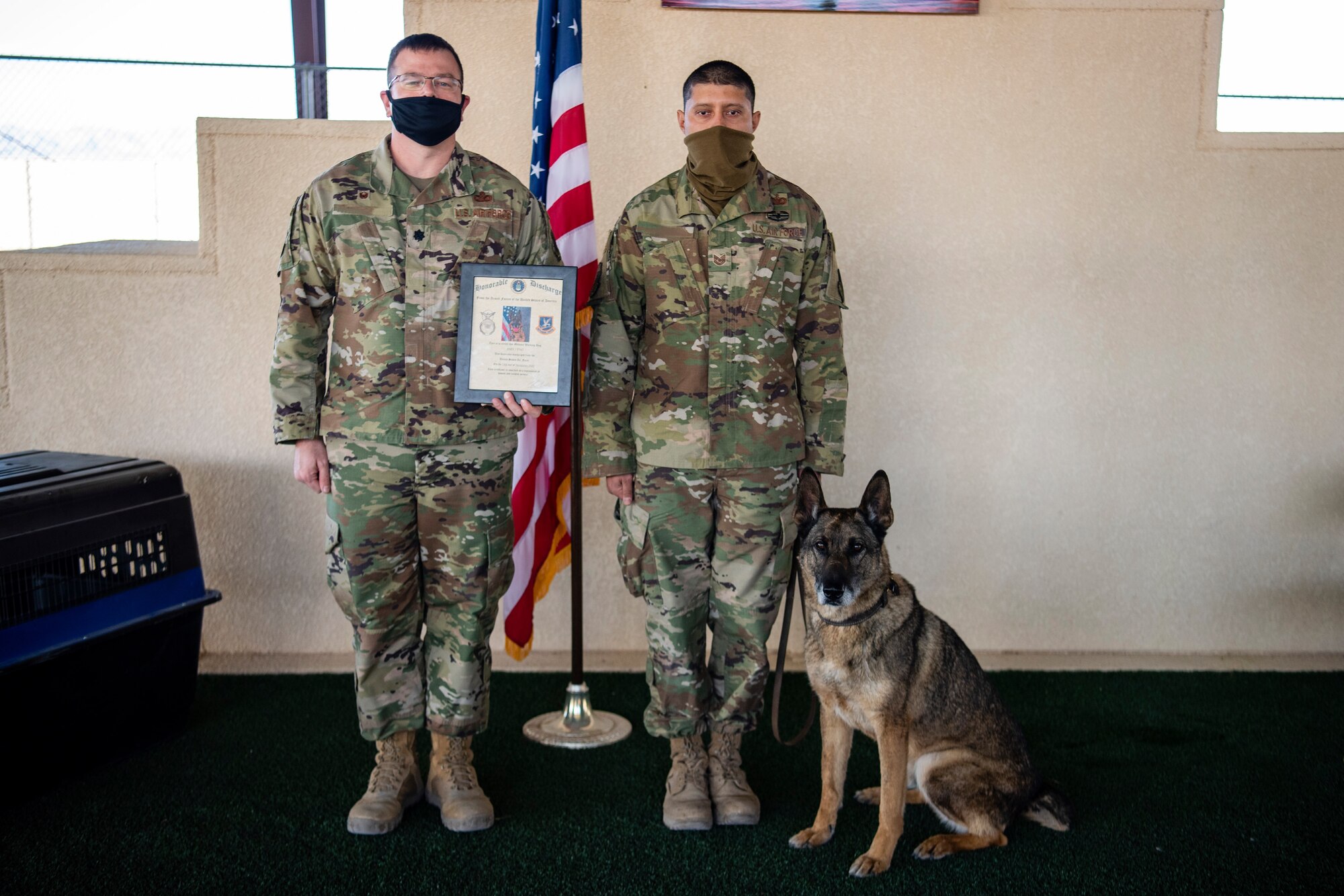 Two security forces members hold a certificate while the military working dog sits by their side.