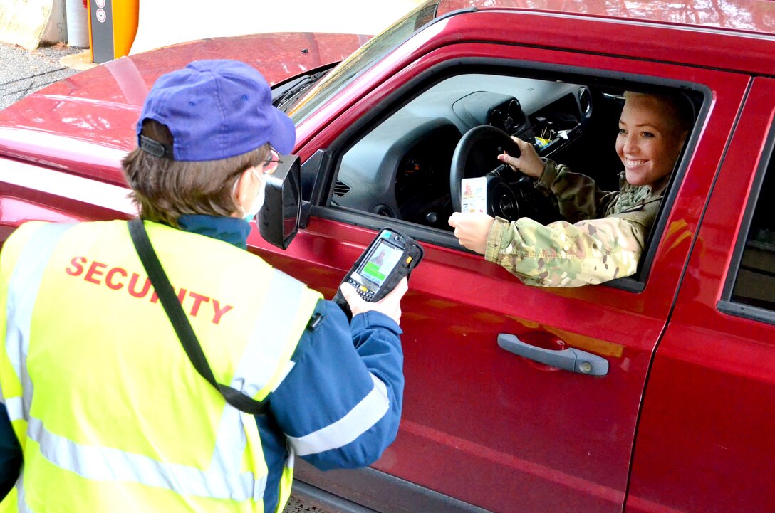 A security guard scans the access card of a soldier sitting in a red truck.