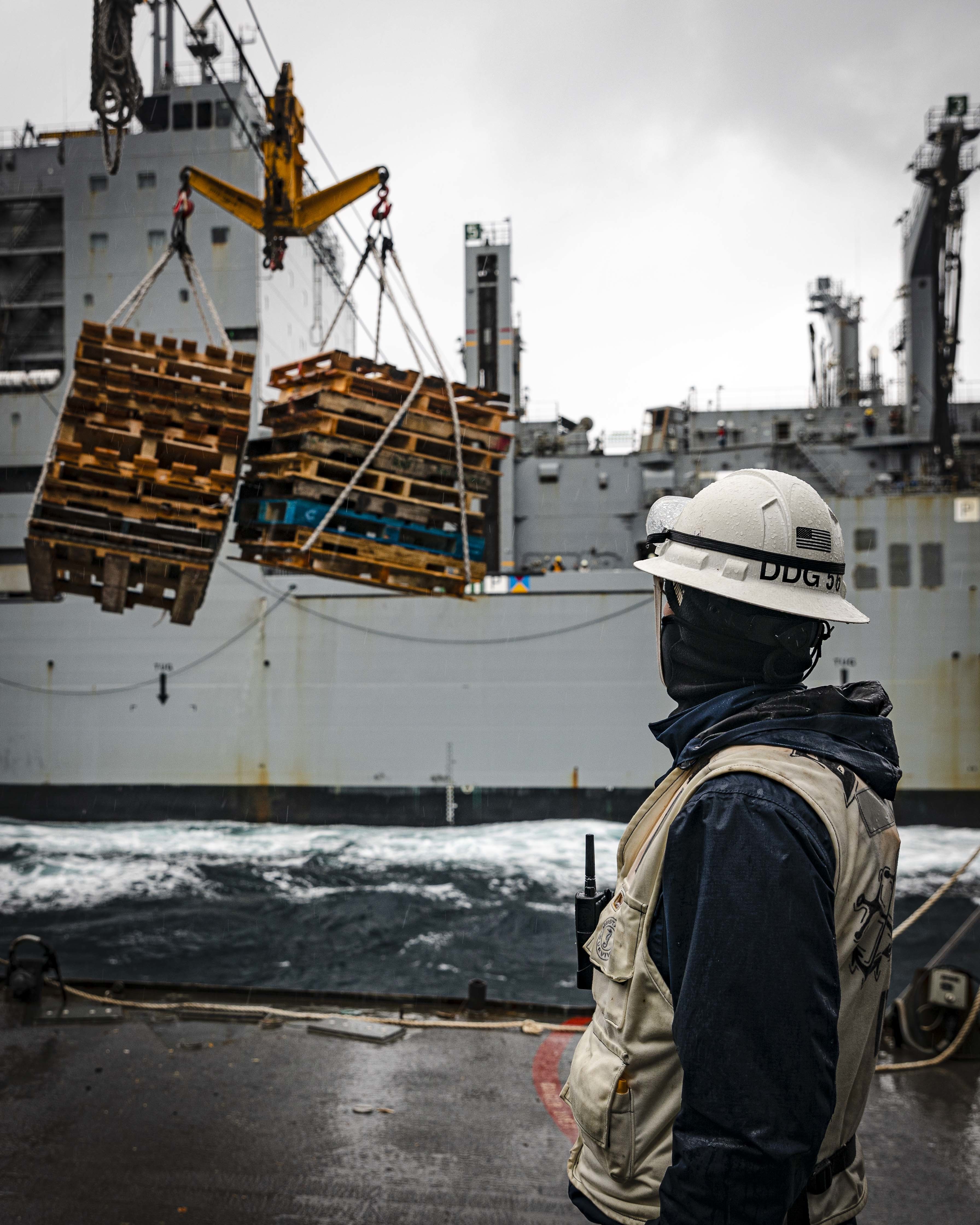 A Sailor observes as a load of pallets transits from USS John S. McCain (DDG 56) to USNS Charles Drew (T-AKE 10) during a replenishment-at-sea.