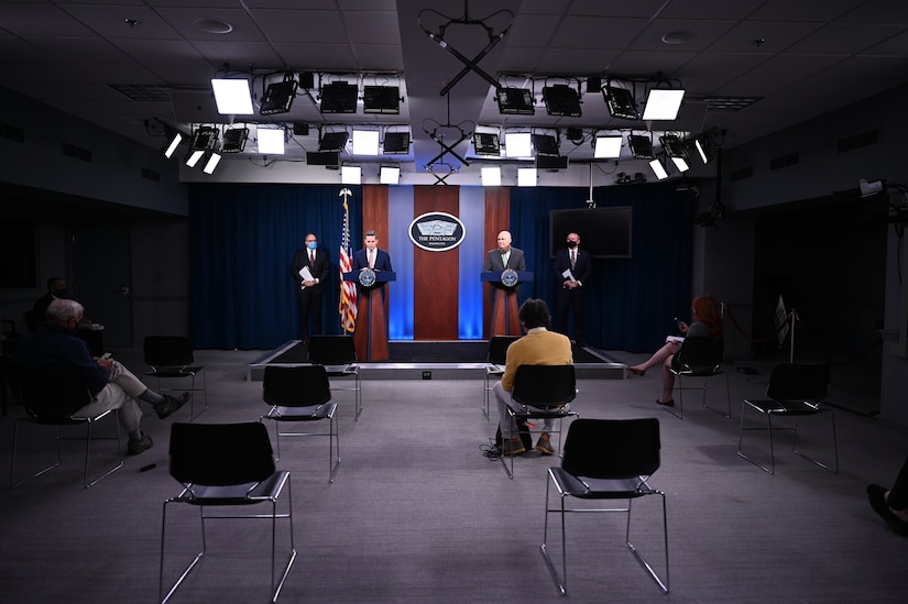 Men stand behind lecterns in a briefing room.