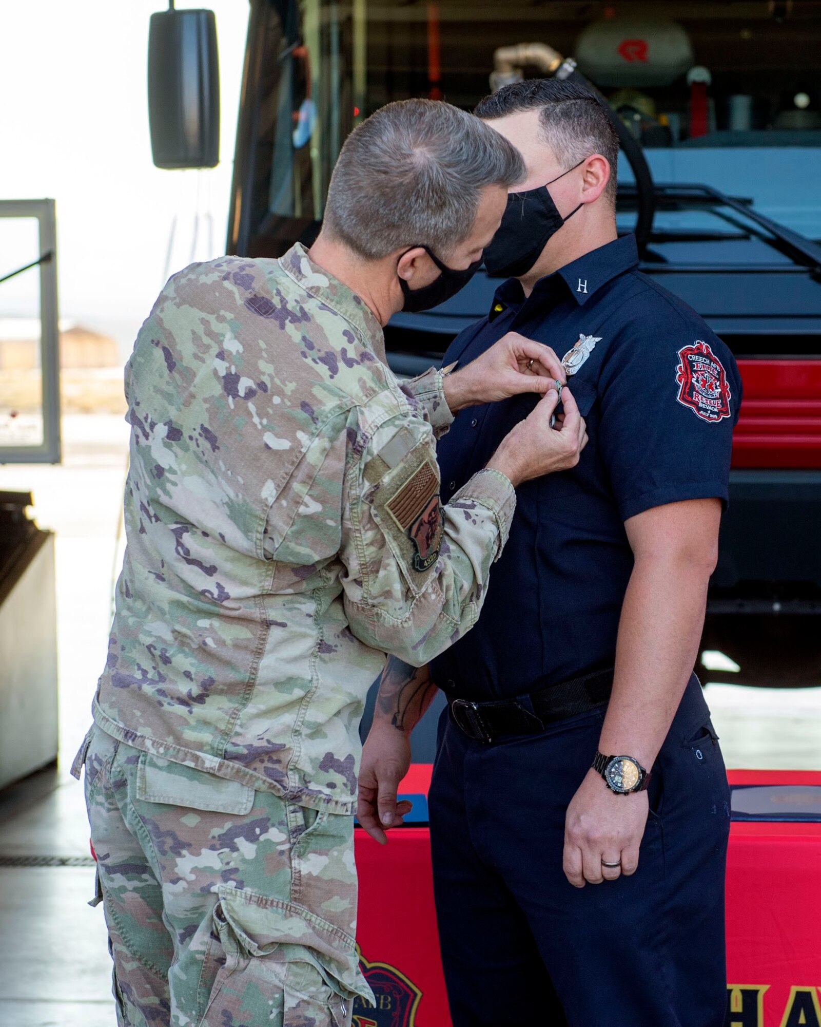 one male colonel in military uniform, pins a medal to the colar of a firefighter while standing in front of a fire truck.