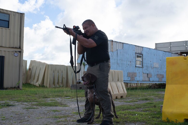 Robert Umadhay, Guam Airport Police Canine Unit, takes aim with Rex in a firing position designed to keep working dogs calm in combat on Andersen Air Force Base, Guam Nov. 20. Guam law enforcement personnel joined service members in military exercises to train advanced skills in a military environment. (U.S. Air Force photo by Staff Sgt. Nicholas Crisp)
