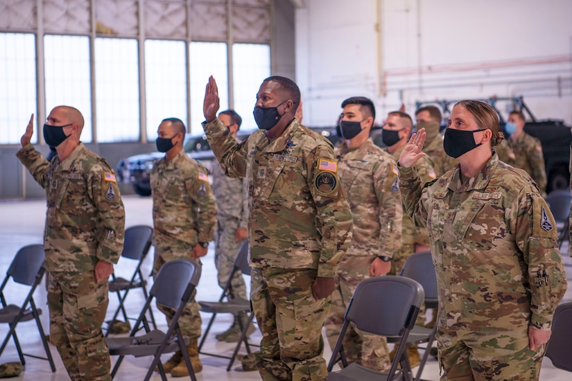 Service members raise hands to swear oaths in hangar.