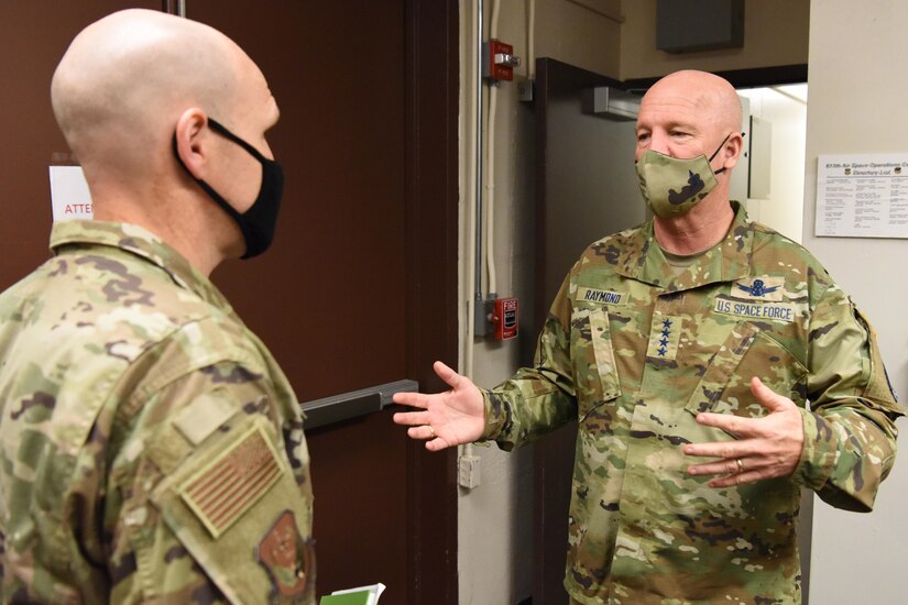 Two men wearing face masks talk in a doorway.