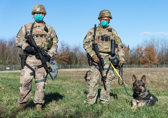Staff Sgt. Brandon Soto and Senior Airman Theresa Braak, both 436th Security Forces Squadron military working dog handlers, along with military working dog Sam, stand guard at a simulated breach in the base’s perimeter fence Nov. 18, 2020, at Dover Air Force Base, Delaware. The exercise entailed 24-hour operations and consisted of an array of scenarios to test the base’s emergency response capabilities, satisfying multiple annual requirements. (U.S. Air Force photo by Roland Balik)