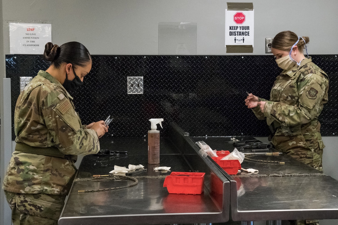 Two female airmen clean weapons while socially distanced.