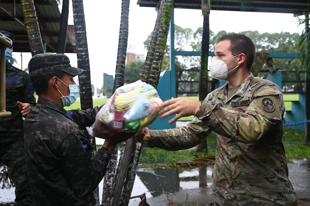 A soldier passes a bundle of food to an airman.