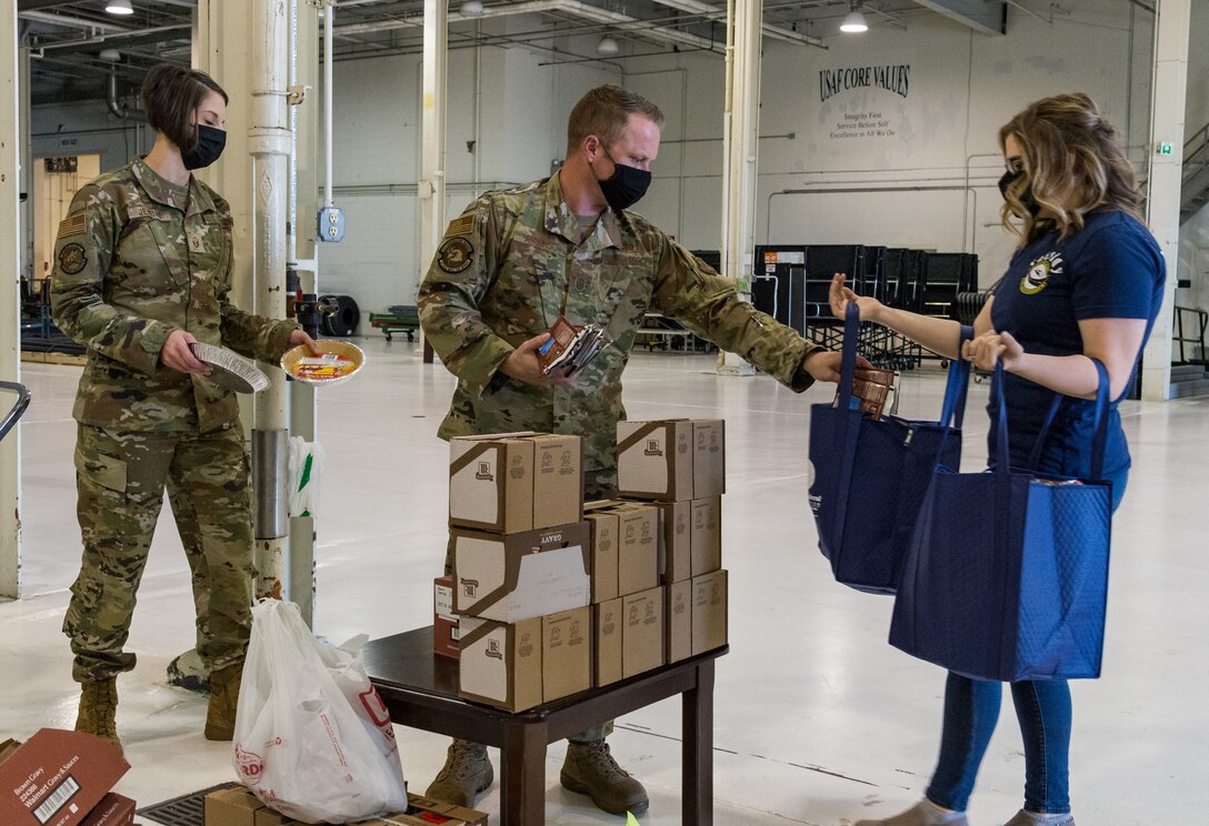 Dover first sergeants Master Sgts. Rebecca Jenkins, 436th Aircraft Maintenance Squadron, and Christopher Anderson, 436th Communications Squadron, place food items in a Thanksgiving holiday food bag held by a volunteer Nov. 20, 2020, at Dover Air Force Base, Delaware. Key spouses, Dover Spouses’ Club members and other volunteers helped fill more than 260 food bags with food items for Team Dover members. Food items were placed in reusable thermal grocery bags donated by the Dover Federal Credit Union. Two frozen whole chickens accompanied each food bag given out. (U.S. Air Force photo by Roland Balik)