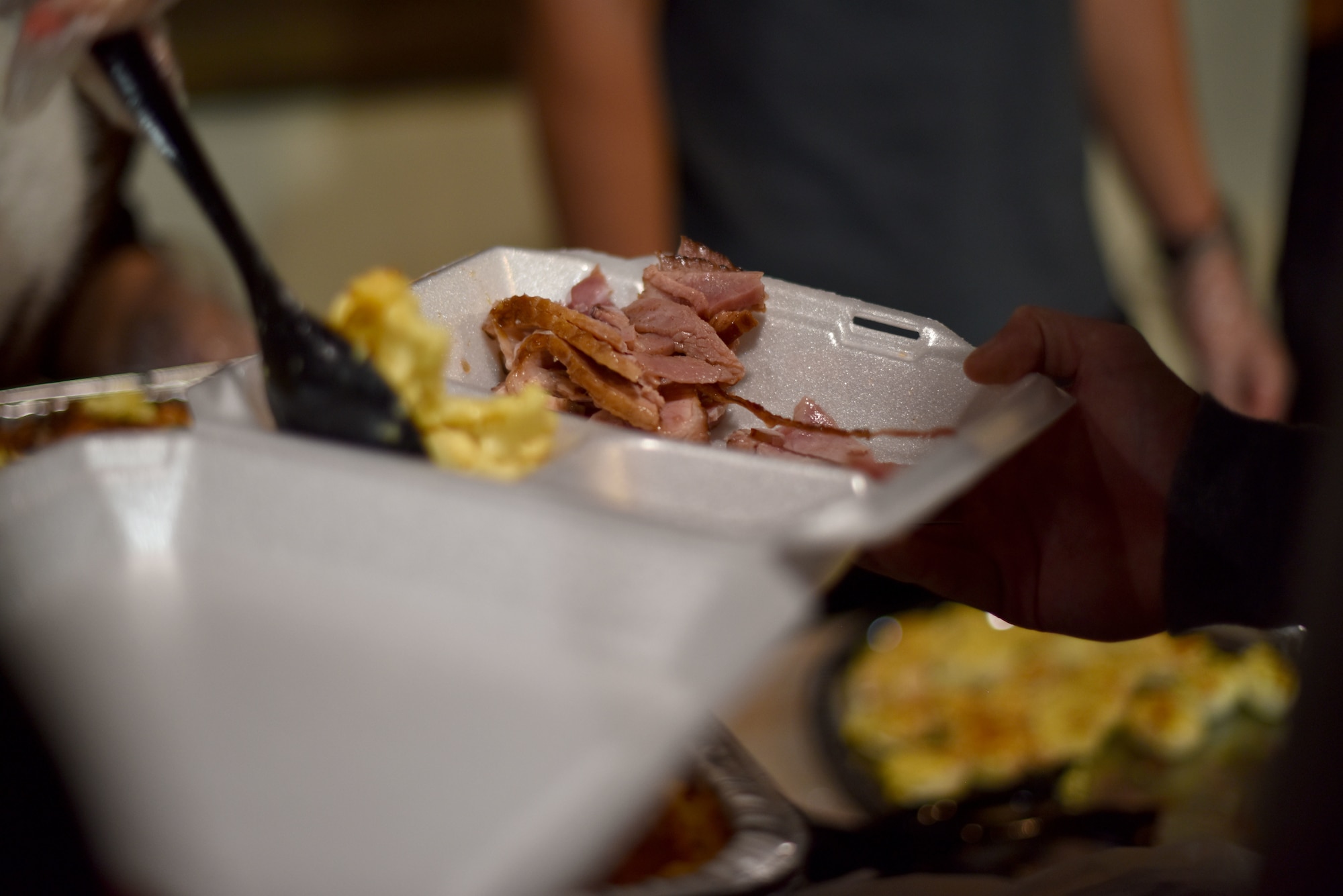 A volunteer serves a student macaroni and cheese during the early Thanksgiving meal hosted at The Crossroads Student Center on Goodfellow Air Force Base, Texas, Nov. 24, 2020. Students had a choice of turkey or ham and a variety of sides. (U.S. Air Force photo by Staff Sgt. Seraiah Wolf)