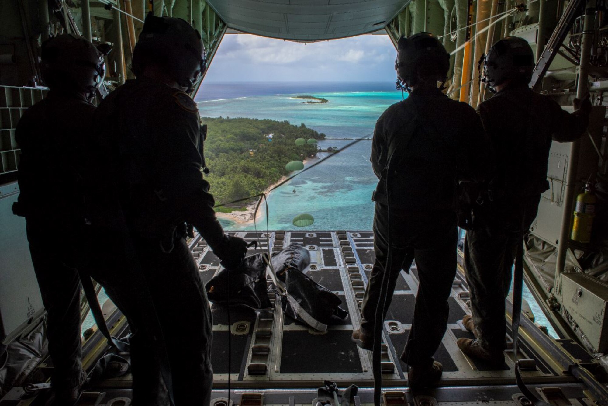 Loadmasters with the 36th Airlift Squadron out of Yokota Air Base, Japan, watch as the four Low-Cost, Low-Altitude humanitarian assistance bundles they just airdropped parachute down to those in need during Operation Christmas Drop 2019, at Nomwin, Federated States of Micronesia, Dec. 13, 2019. During 2020, Airmen will take strict measures to mitigate the transmission of COVID-19. Participating Airmen will wear a mask, wash their hands and practice social distancing. (U.S. Air Force photo by Senior Airman Matthew Gilmore)