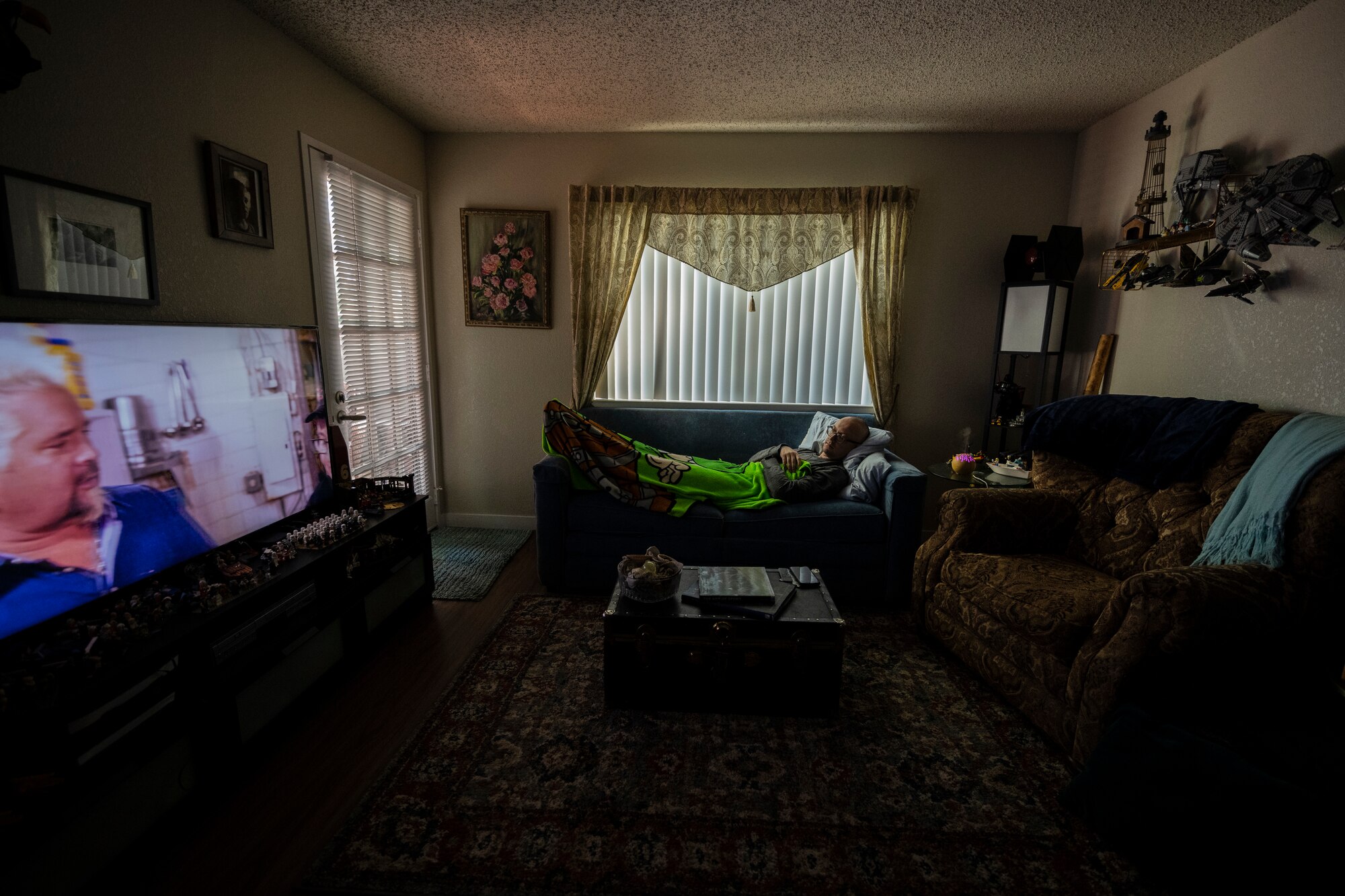 A man lays on his couch and watches a cooking show on TV.