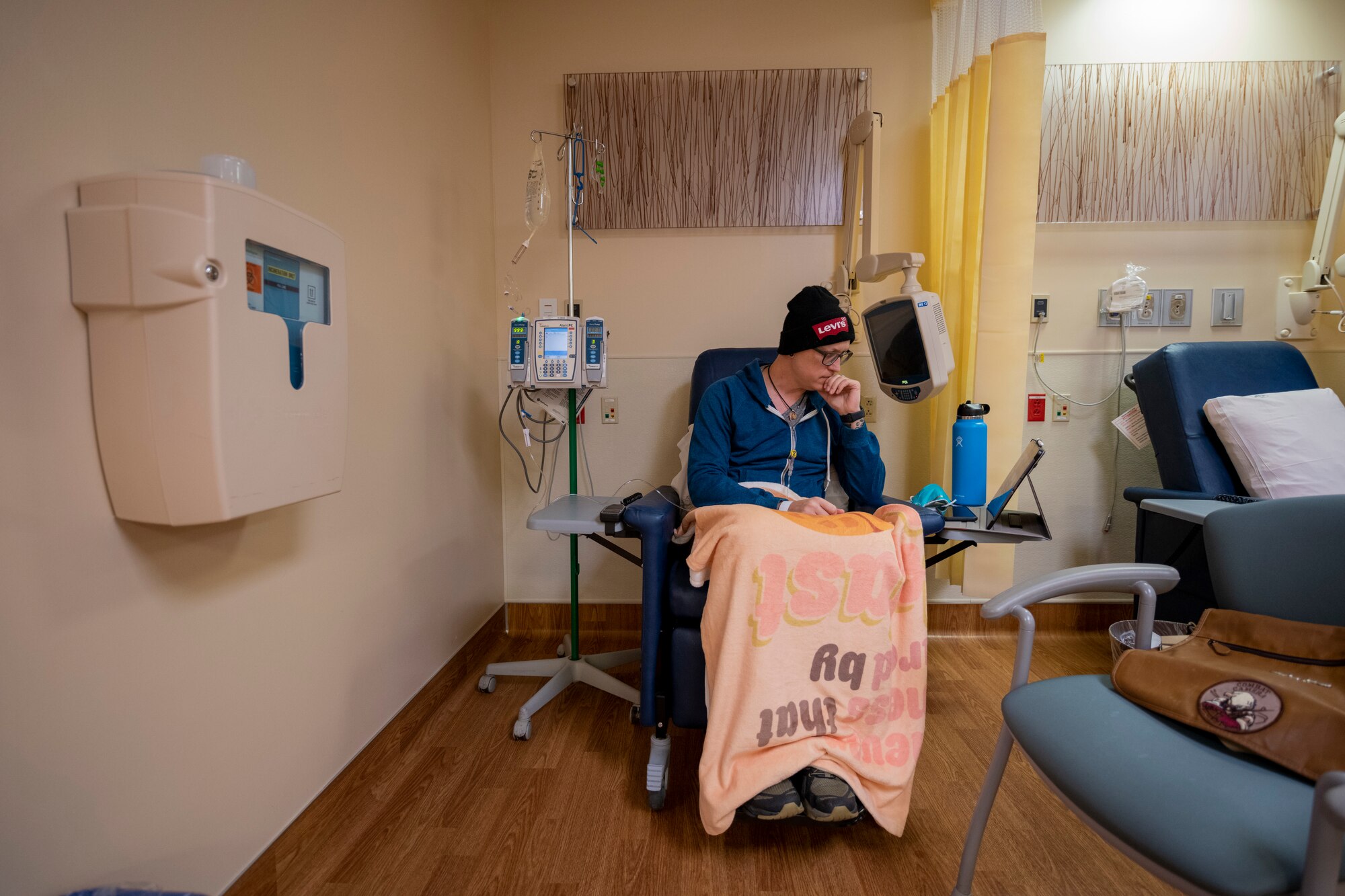 A man sits in a chair with tubes connected to his body while he receives chemotherapy.