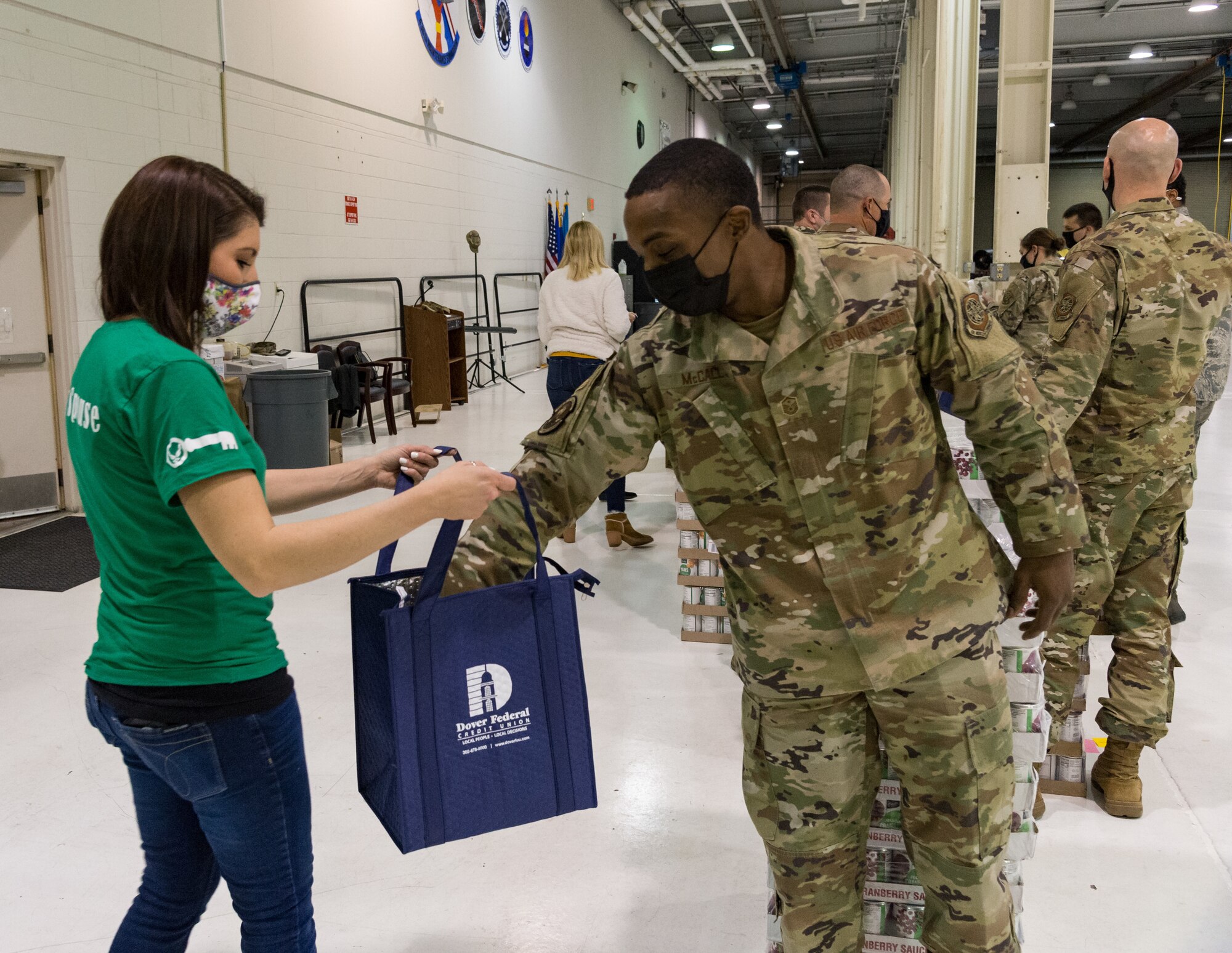 Master Sgt. Maurious McCall, 436th Security Forces Squadron first sergeant, places a food item in a Thanksgiving holiday food bag held by Lynne Otis, 436th Airlift Wing Staff Agencies key spouse, Nov. 20, 2020, at Dover Air Force Base, Delaware. Key spouses, Dover Spouses’ Club members and other volunteers helped fill more than 260 food bags with food items for Team Dover members. Food items were placed in reusable thermal grocery bags donated by the Dover Federal Credit Union. Two frozen whole chickens accompanied each food bag given out. (U.S. Air Force photo by Roland Balik)