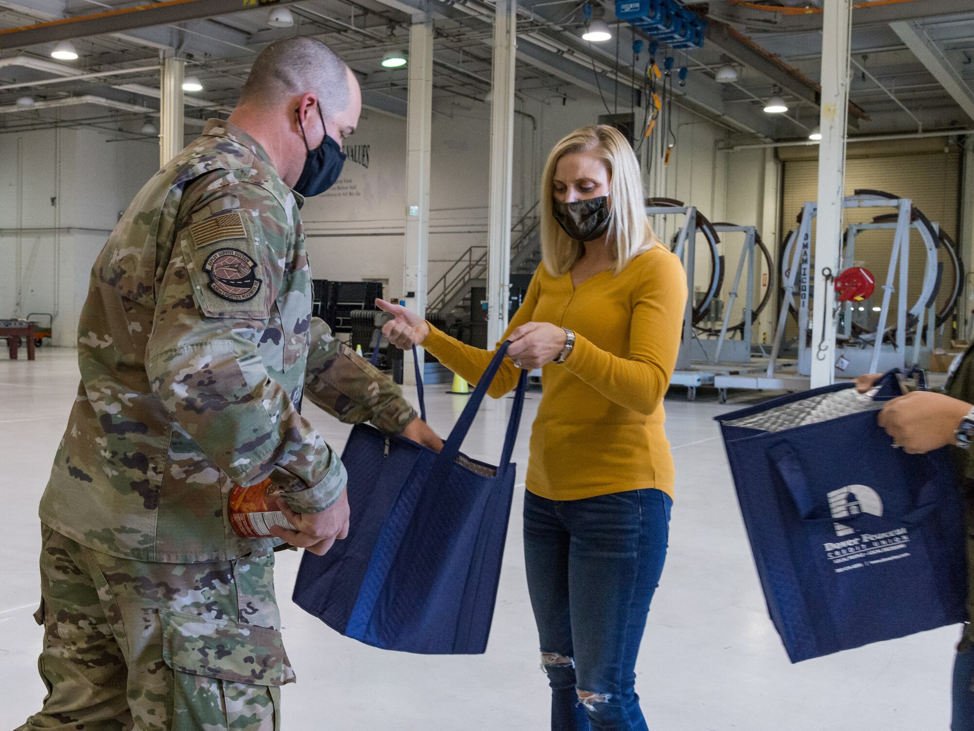 Master Sgt. Matthew Morrison, 436th Logistics Readiness Squadron first sergeant, places a nonperishable food item in a Thanksgiving holiday food bag held by Christie Jones, wife of Col. Matthew Jones, 436th Airlift Wing commander Nov. 20, 2020, at Dover Air Force Base, Delaware. Key spouses, Dover Spouses’ Club members and other volunteers helped fill more than 260 food bags with food items for Team Dover members. Food items were placed in reusable thermal grocery bags donated by the Dover Federal Credit Union. Two frozen whole chickens accompanied each food bag given out. (U.S. Air Force photo by Roland Balik)
