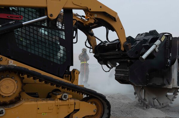 A U.S. Air Force Airman from the 386th Expeditionary Civil Engineer Squadron prepares to clear the area of debris while a saw-equipped compact track loader cuts through concrete during a Rapid Airfield Damage Recovery training exercise at Ali Al Salem Air Base, Kuwait, Nov. 16, 2020. The saw cuts along a previously marked area surrounding a damaged portion of the runway to help with the repairs. (U.S. Air Force photo by Staff Sgt. Kenneth Boyton)