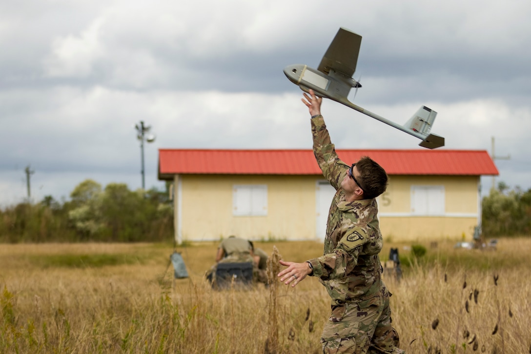 A soldier launches an unmanned aerial vehicle from a field.