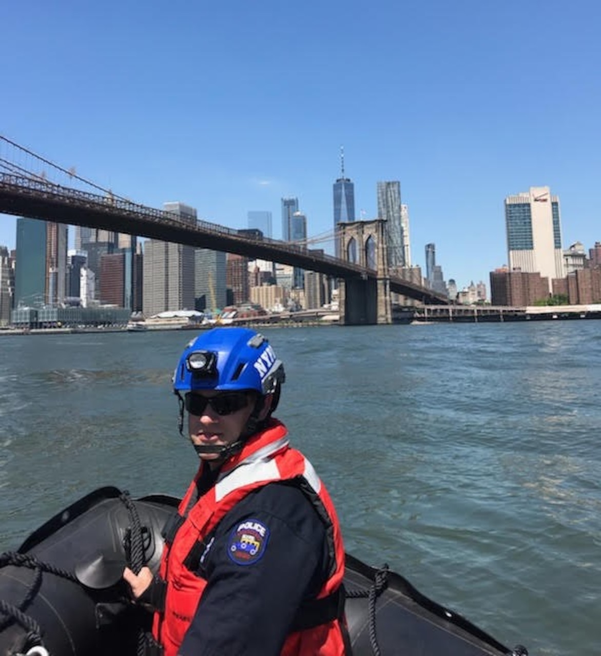 A man floats in a boat near a bridge; a city skyline is in the background.