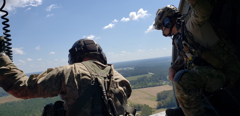 Two men look out onto farmland from an open helicopter door.