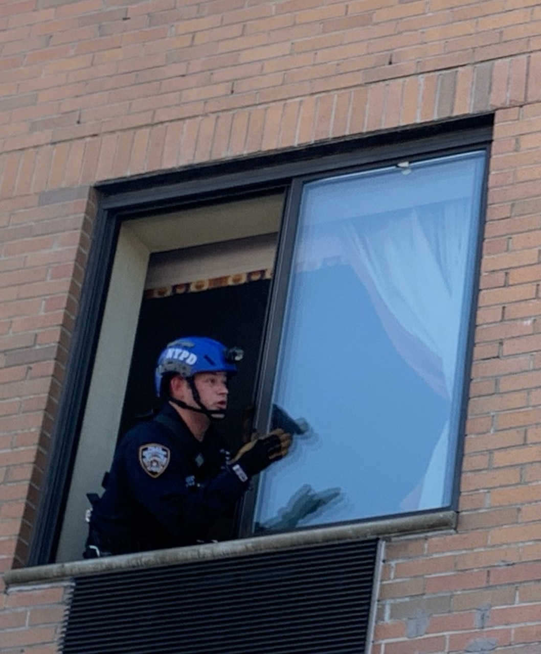 A man in an NYPD helmet talks to someone through an open window.